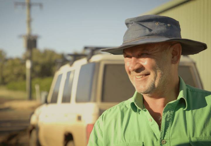 Farmer in green shirt wearing a hat standing outside at his farm with 4WD in the background