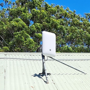 A rectangular-shaped antenna with rounded edges, known as an nbn Wireless Network Terminating Device Version 4, on a house roof with trees in the background